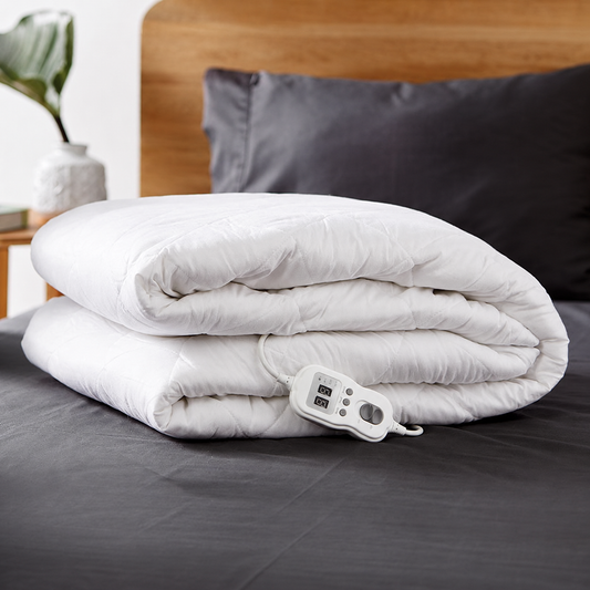 Folded white quilted electric blanket resting on a bed